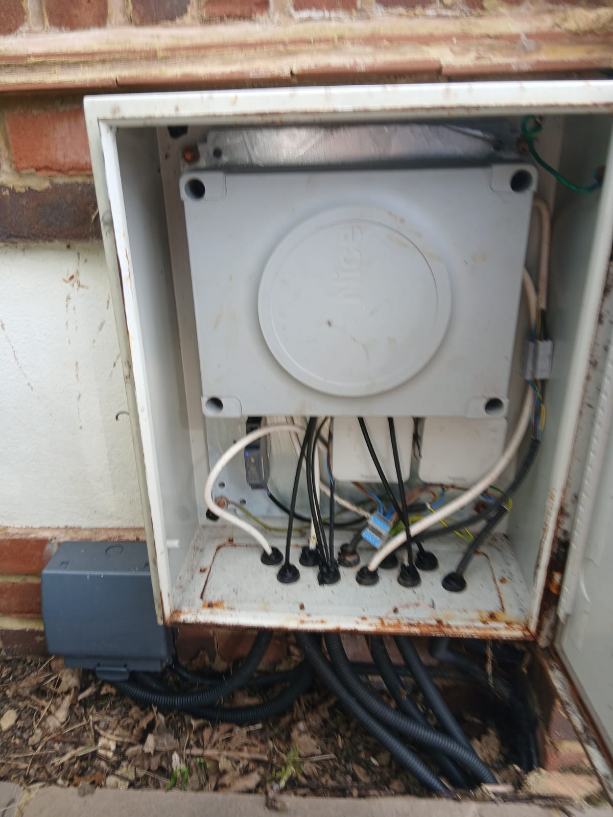 Rusted outdoor gate control box with cables forced through unsealed holes, water and corrosion